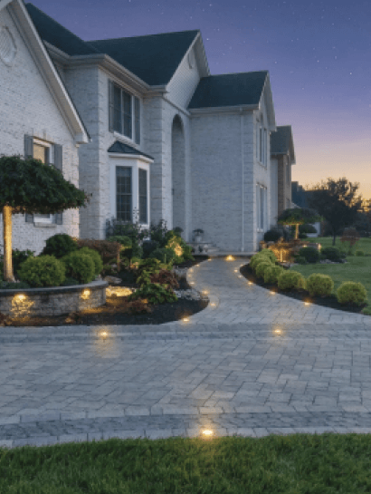 Pale brick colonial home with a curved paver walkway lined by warm path lights at twilight